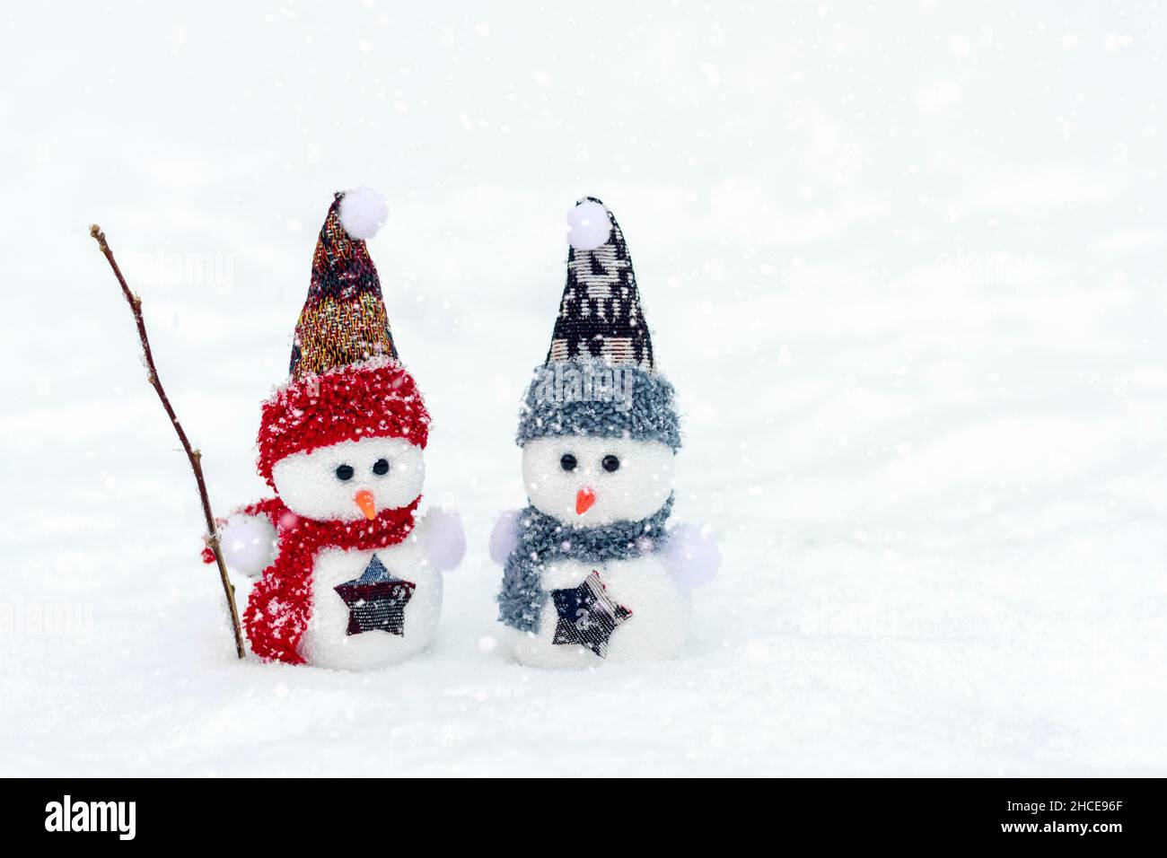 Joyeux noël et bonne année carte de voeux avec espace copie deux petits bonshommes de neige heureux en rouge, bleu casquette et écharpe debout dans le fond de neige d'hiver Banque D'Images