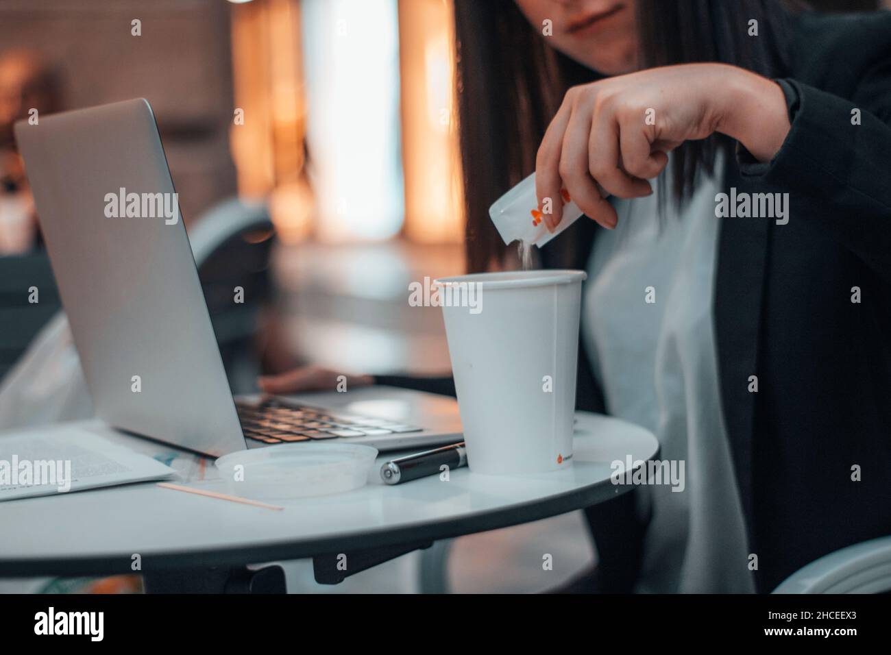 Une jeune femme de direction verse du sucre dans un café dans une cafétéria de la place de la ville tout en travaillant avec son ordinateur portable Banque D'Images