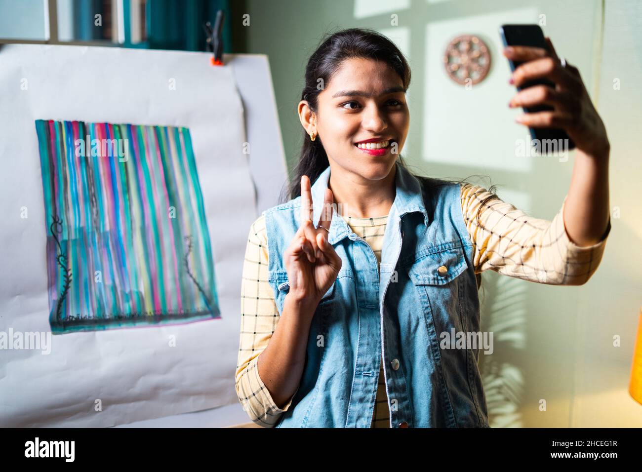 Femme artiste professionnelle prenant selfie devant sa peinture avec la victoire ou le signe v pour partager sur les médias sociaux ou Internet - concept de Hobby Banque D'Images