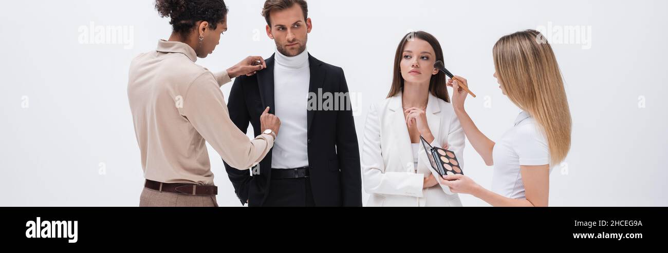 jeune styliste interracial et maquilleur préparant des modèles professionnels à séance photo isolée sur blanc, bannière Banque D'Images