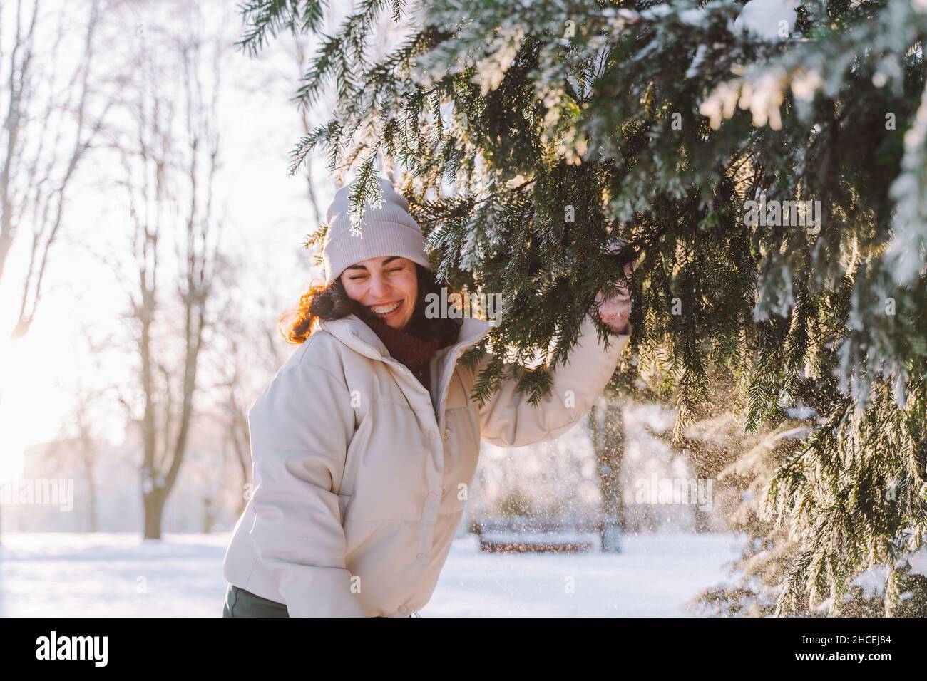 Une jeune femme souriante et carie se promet se cache derrière un sapin de Noël recouvert de neige.Émotions positives, fraîcheur, vacances. Banque D'Images