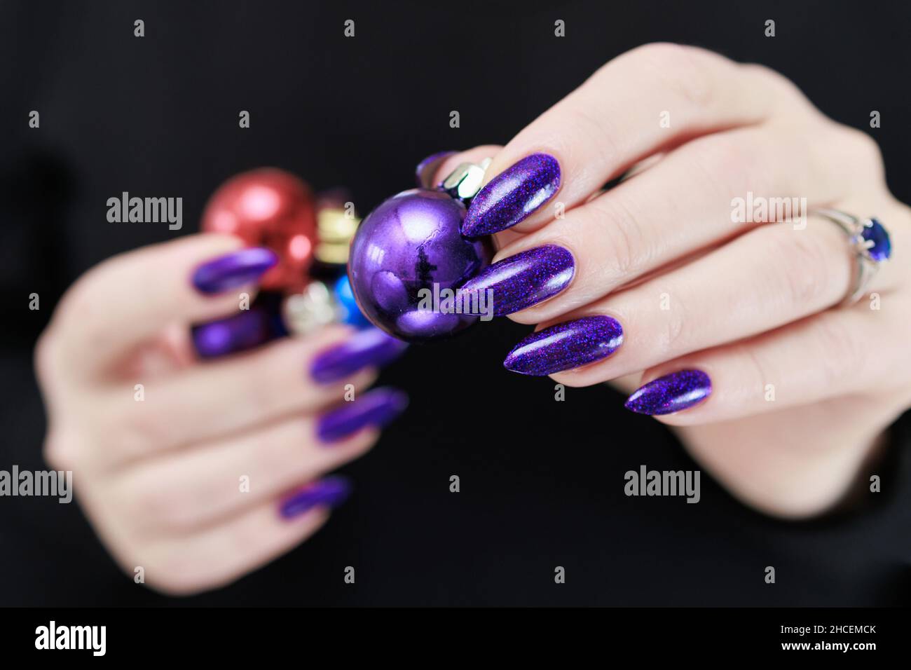 Les mains de femmes avec de longs ongles et une manucure violet et bleu vif  tiennent une boîte-cadeau et des boules de Noël.Félicitations à la nouvelle  année et à Noël Photo Stock -