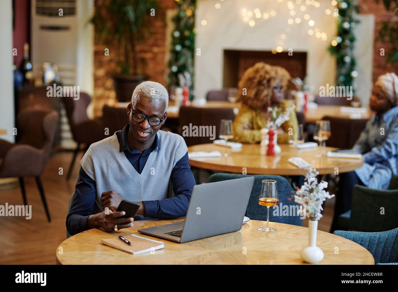 Un jeune homme d'affaires heureux lisant un message sur un téléphone portable tout en étant assis à la table avec un ordinateur portable dans un café Banque D'Images