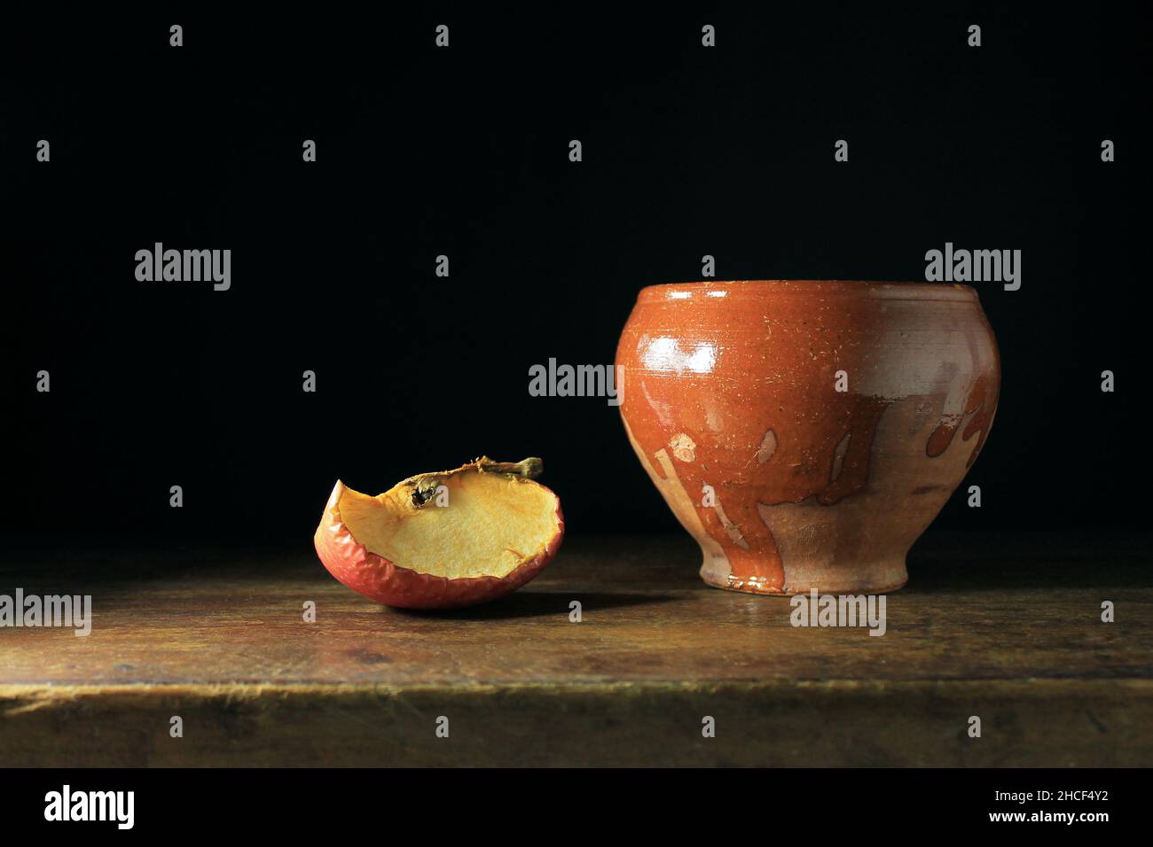 Encore la vie avec une partie d'une pomme, un vase en faïence sur une table en bois, et un fond noir Banque D'Images