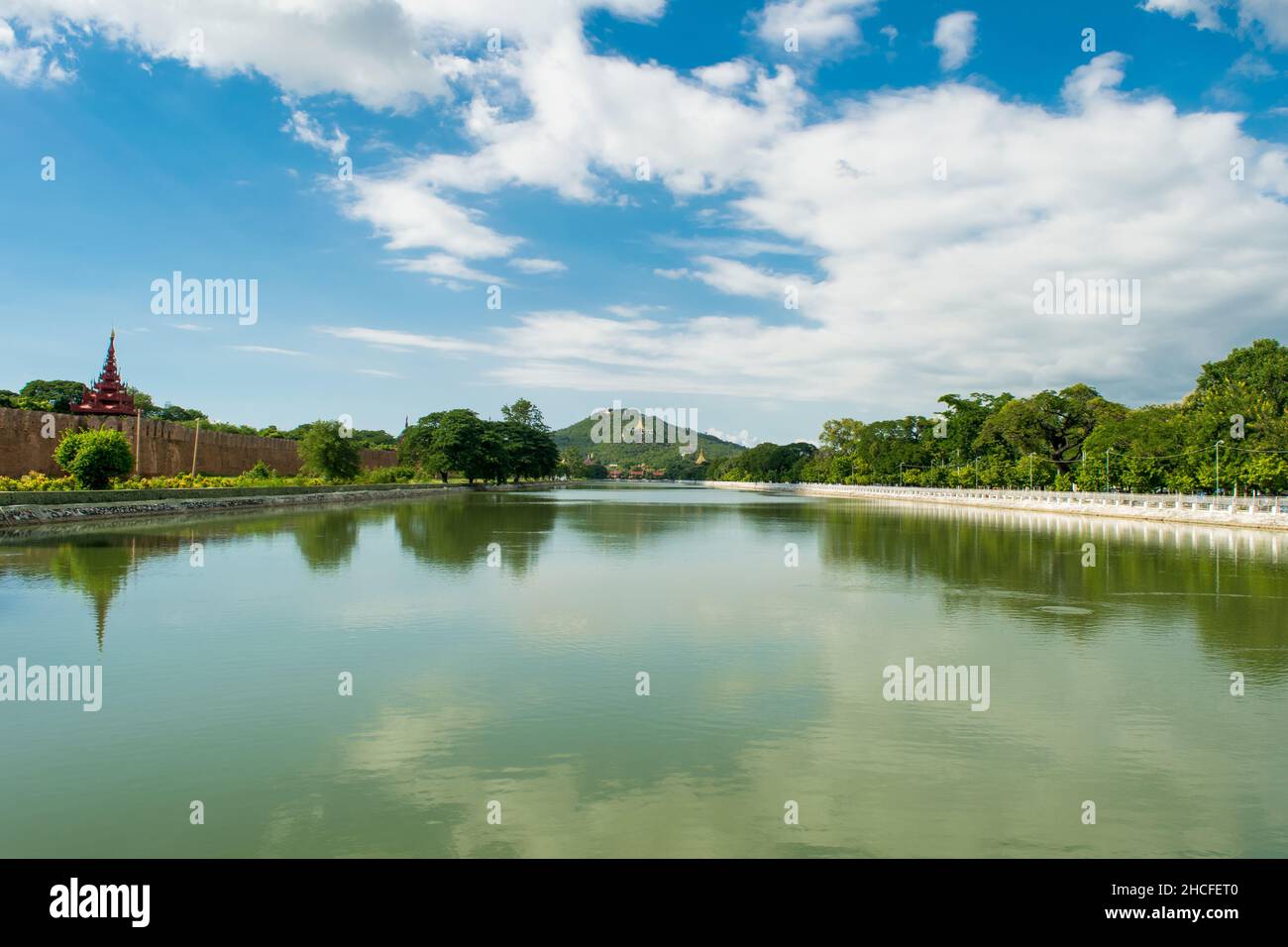 Une grande piscine d'eau réfléchissante, avec une vue lointaine sur la colline de Mandalay, sur un ciel bleu et nuageux Banque D'Images