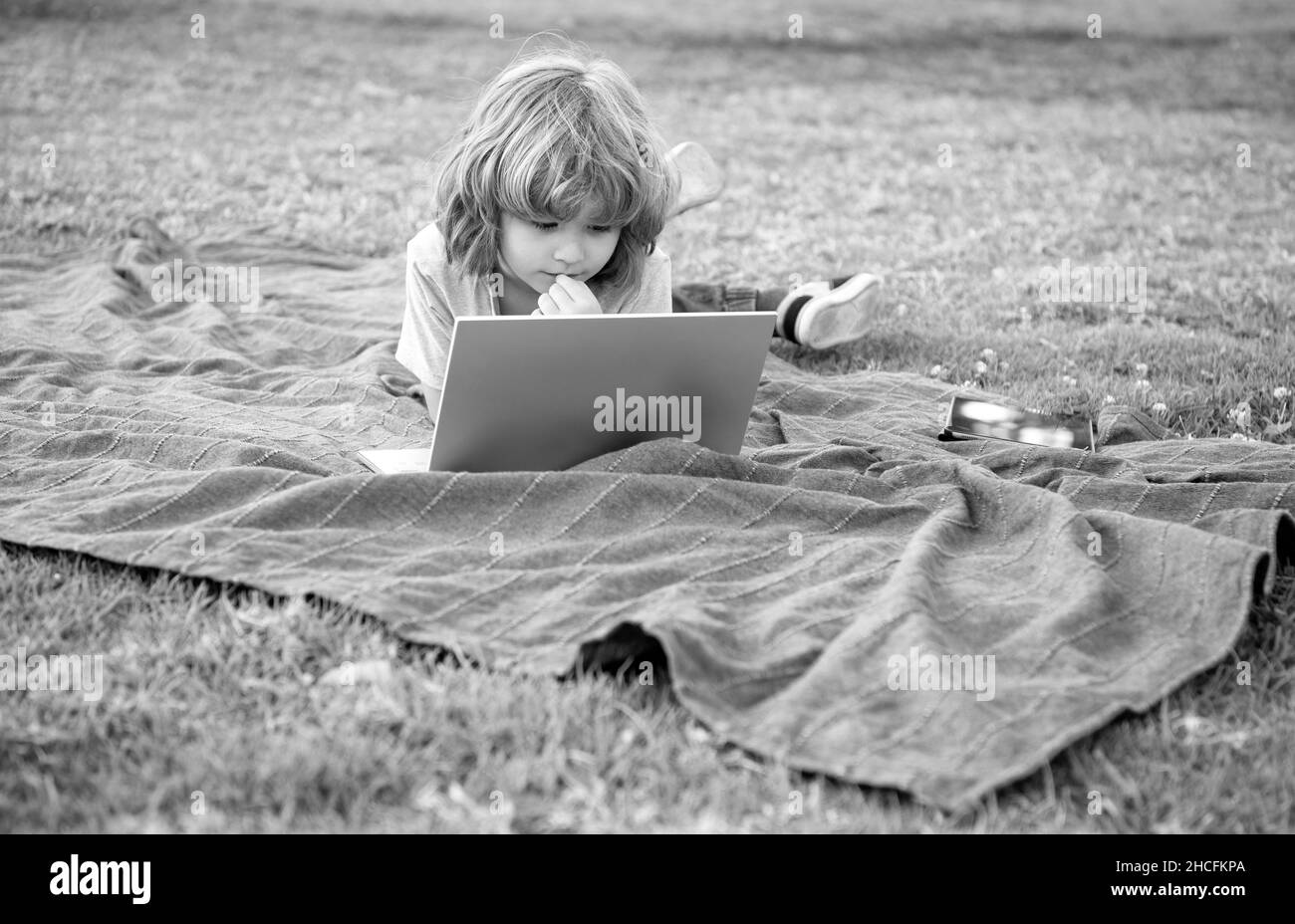 Garçon enfant surfer sur Internet dans ordinateur portable se détendre sur une couverture naturelle à l'extérieur, l'éducation à distance Banque D'Images