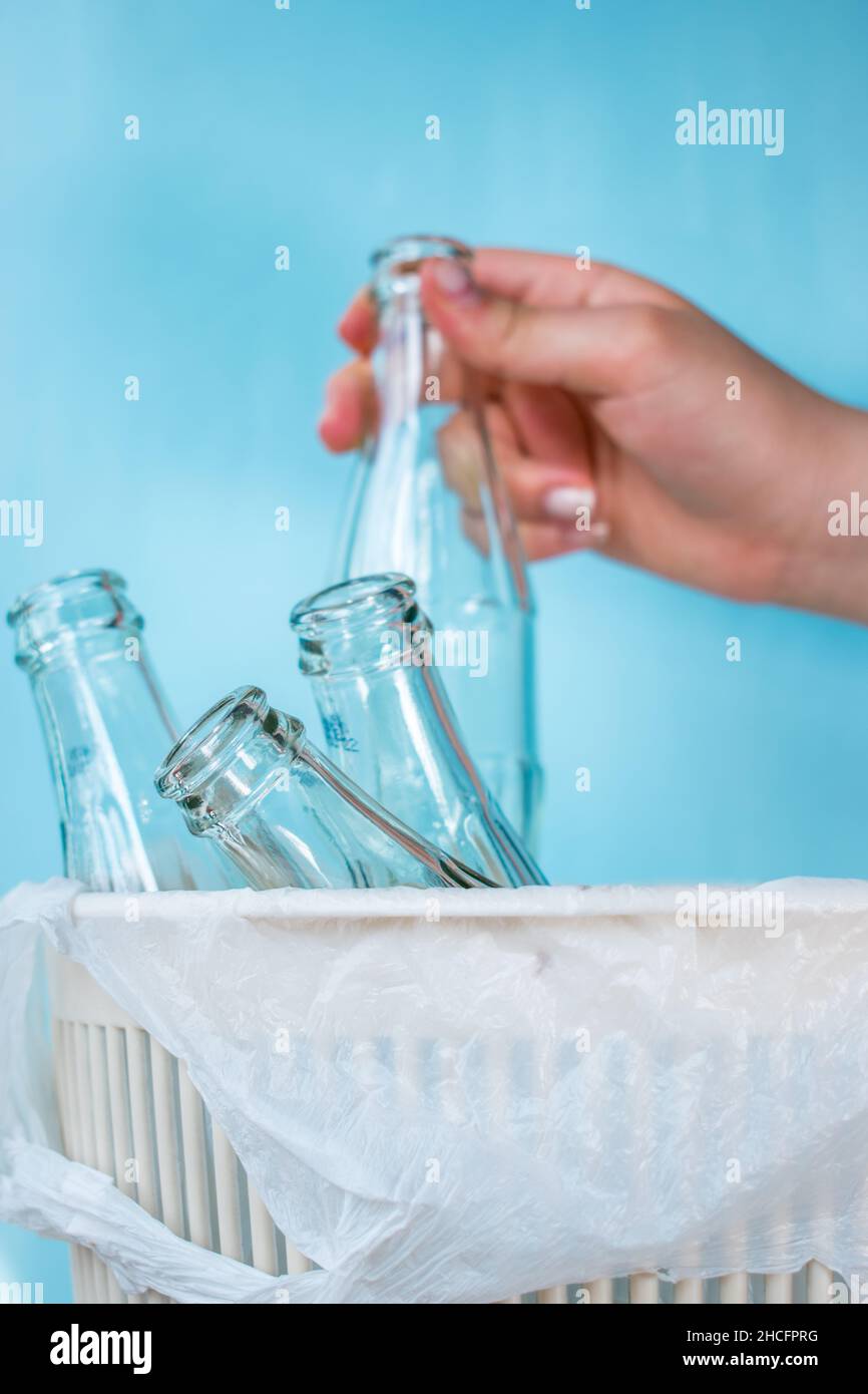 Main tenant une bouteille en verre dans un bac de recyclage qui a un sac blanc sur fond bleu clair Banque D'Images