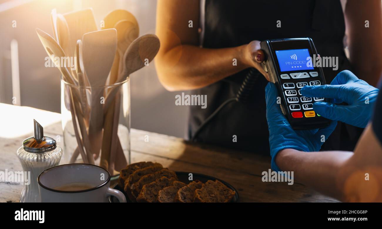 Serveur tenant la machine à glisser de carte de crédit pendant que le client avec des gants tapant le code PIN.Femme effectuant le paiement à la cafétéria avec carte de crédit.Paiement par le client Banque D'Images