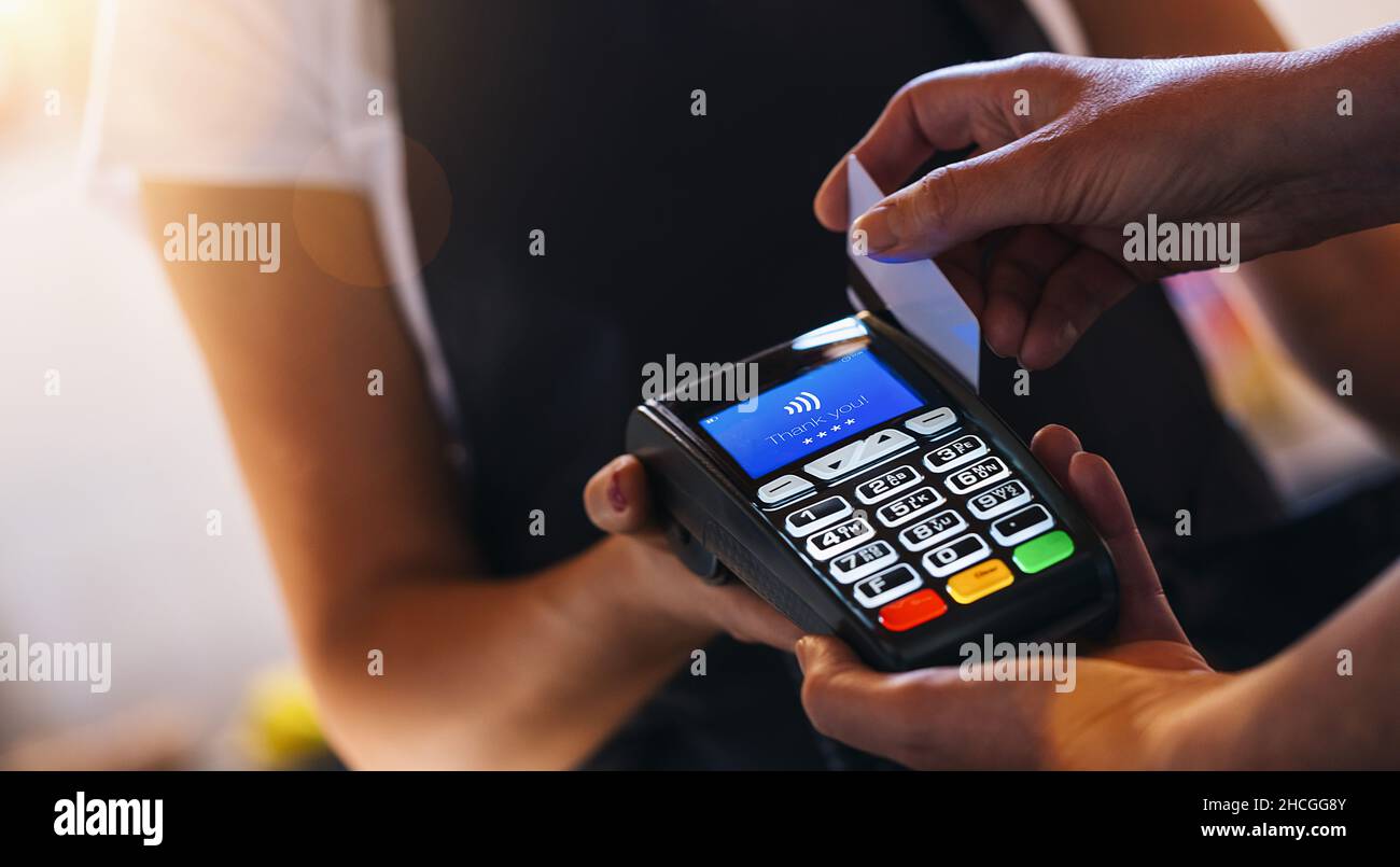 Serveur tenant la machine à glisser la carte de crédit pendant que le  client fait glisser la carte.Femme effectuant le paiement à la cafétéria  avec carte de crédit.Client payant pour le café