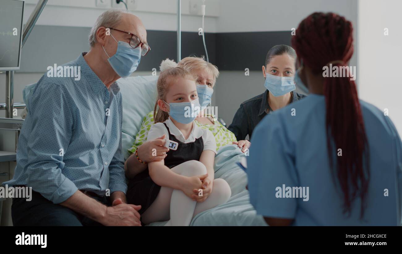 Infirmière donnant des conseils de rétablissement au patient et aux visiteurs ayant un masque facial dans la salle d'hôpital.Assistant médical aidant avec les médicaments lors de la visite de contrôle, parlant à la femme malade et à la famille pendant la pandémie. Banque D'Images