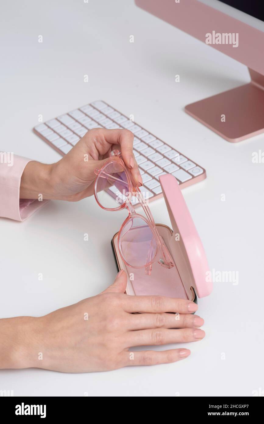 Angleterre, Royaume-Uni.2021. Les mains des femmes enlever les lunettes de l'étui avec un fond d'ordinateur et de clavier, tous roses. Banque D'Images