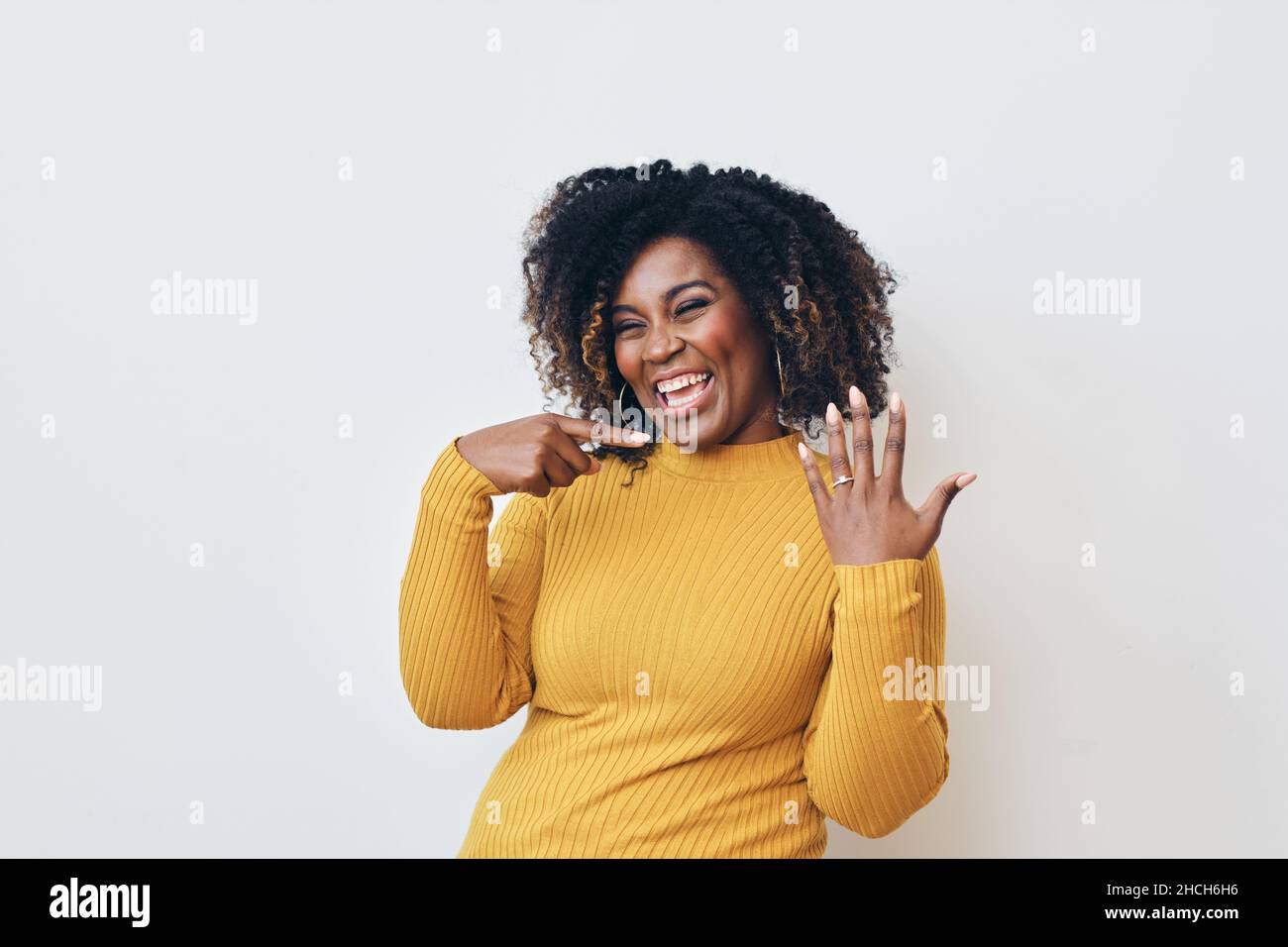Femme joyeuse avec une coiffure frisée sur fond blanc.Sourire.En regardant la caméra montrant l'anneau d'engagement Banque D'Images
