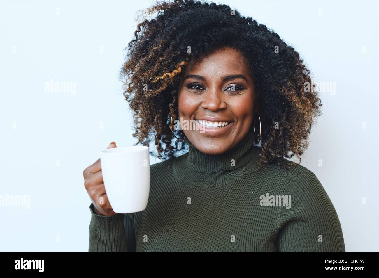 Femme afro-américaine souriante, adulte, aux cheveux bouclés tenant une tasse blanche Banque D'Images