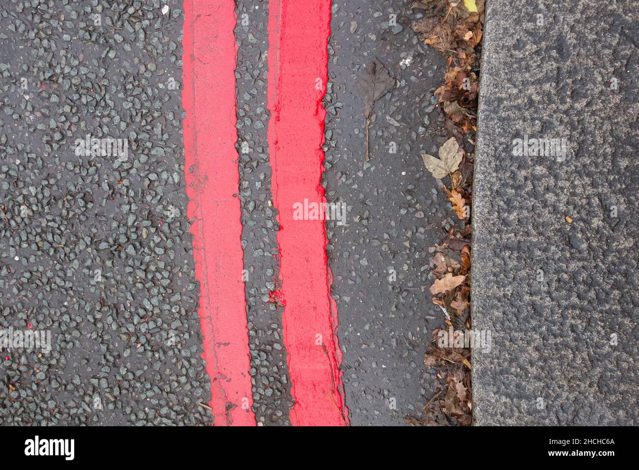 Gros plan des marquages routiers à deux lignes rouges indiquant un itinéraire rouge et que les règles et réglementations s'appliquent à tout moment et tous les jours Banque D'Images