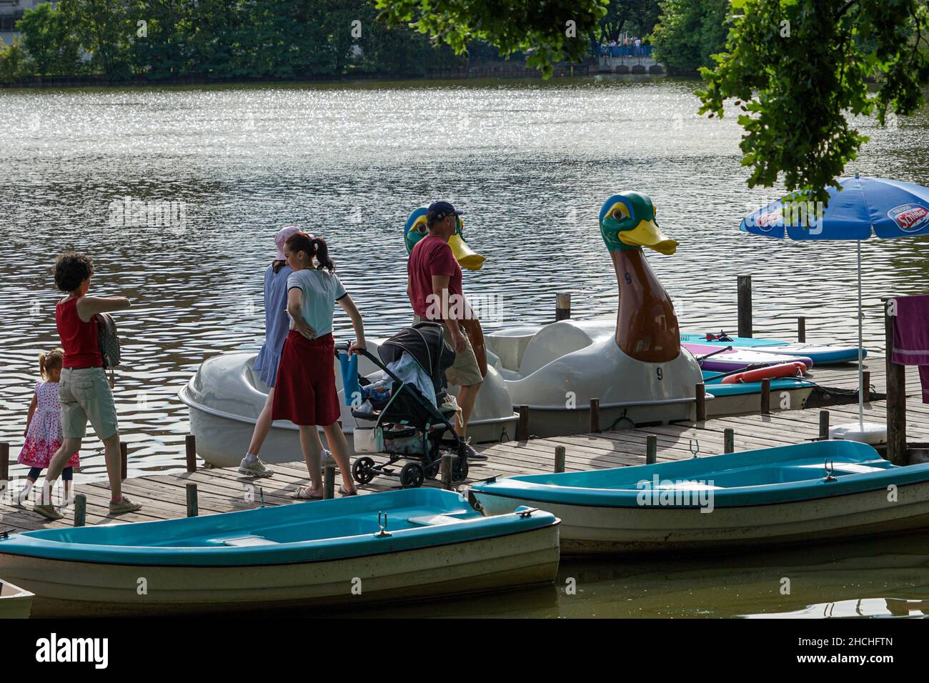 Une famille avec un enfant et un bébé dans un pram marche le long d'un quai où des bateaux à pédales et des bateaux à pédales d'animaux attendent les clients. Banque D'Images