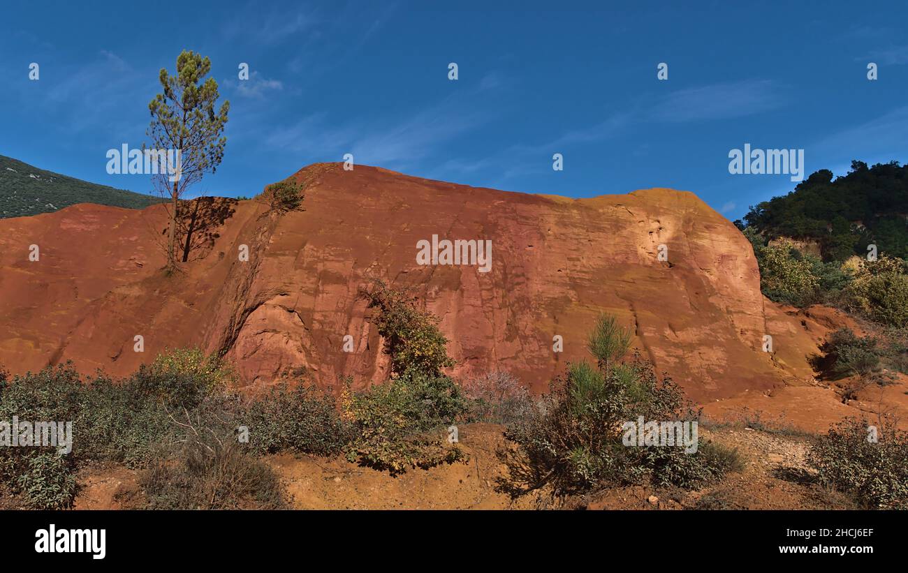 Vue imprenable sur les rochers ocre orange et rouge du Colorado provençal avec des buissons verts et des arbres près de Rustrel dans la vallée du Luberon, Provence, France. Banque D'Images