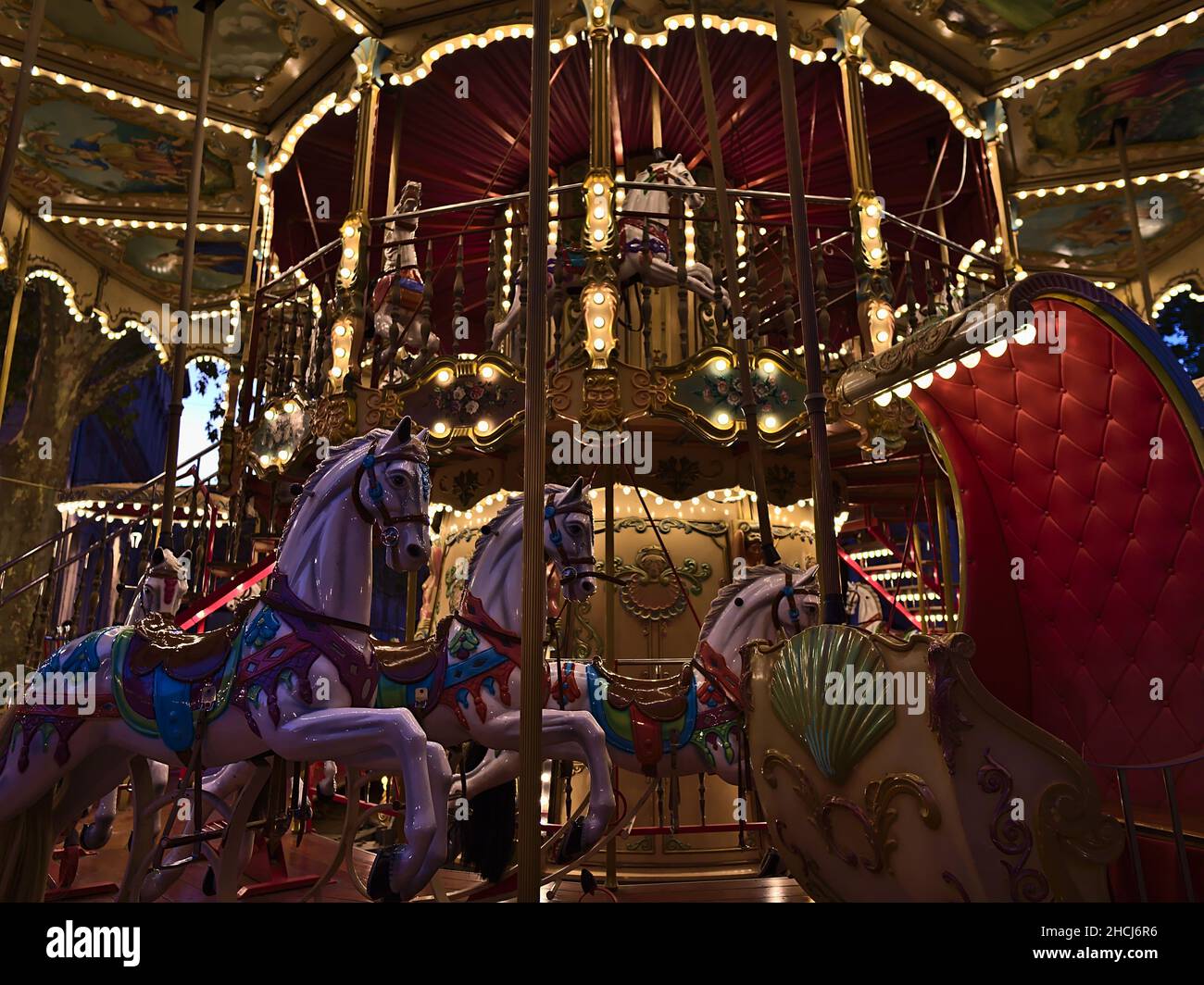 Vue rapprochée d'un manège illuminé pour les enfants dans le centre d'Avignon, Provence, France en soirée avec des chevaux colorés décorés. Banque D'Images
