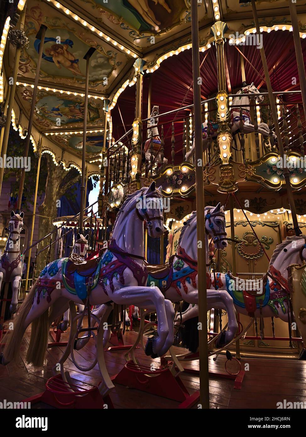 Vue rapprochée d'un manège illuminé pour les enfants dans le centre d'Avignon, Provence, France en soirée avec des chevaux colorés décorés. Banque D'Images