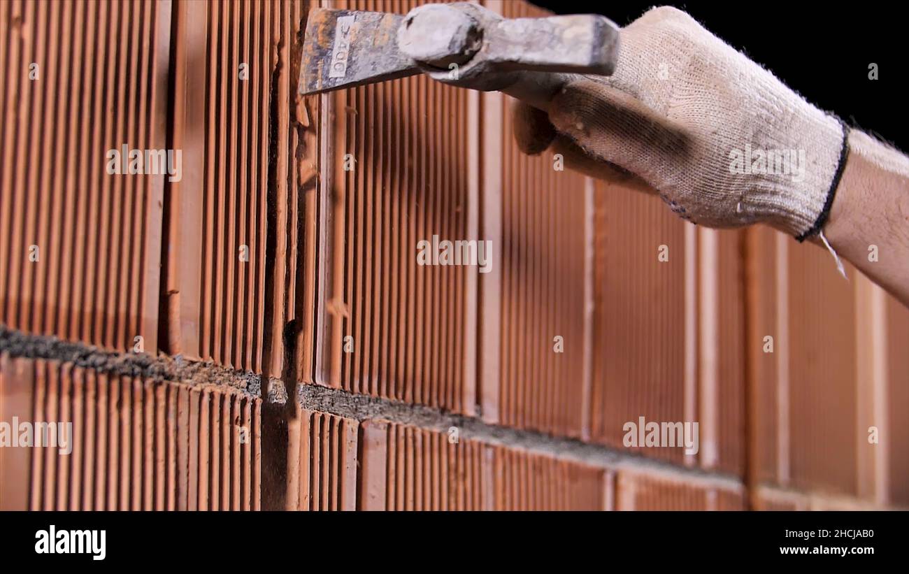 Gros plan d'un homme martelant le mur en blocs de céramique sur le chantier de construction.Porter des gants de protection pour percer un trou dans le mur. Banque D'Images