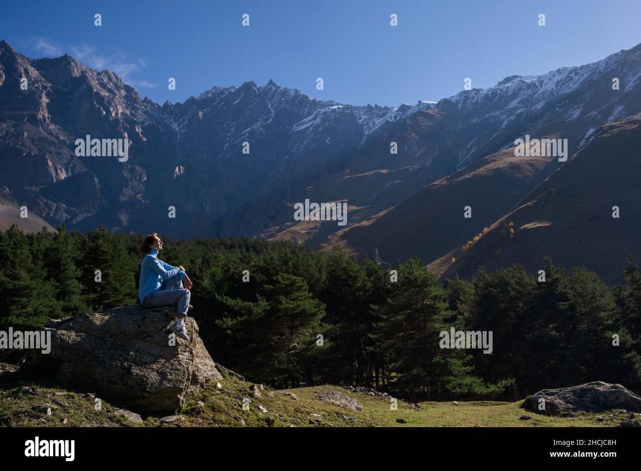 Femme reposant sur le rocher contre la chaîne de montagnes. Parc national de Kazbegi, Dariali, Géorgie. Banque D'Images