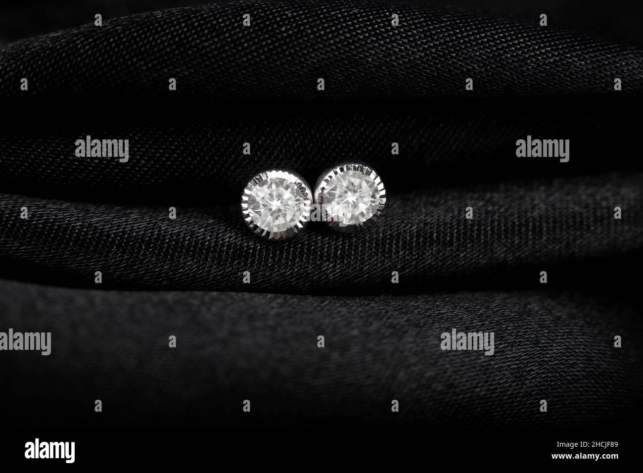 Puces d'oreilles rondes en argent avec losange sur fond noir. Banque D'Images