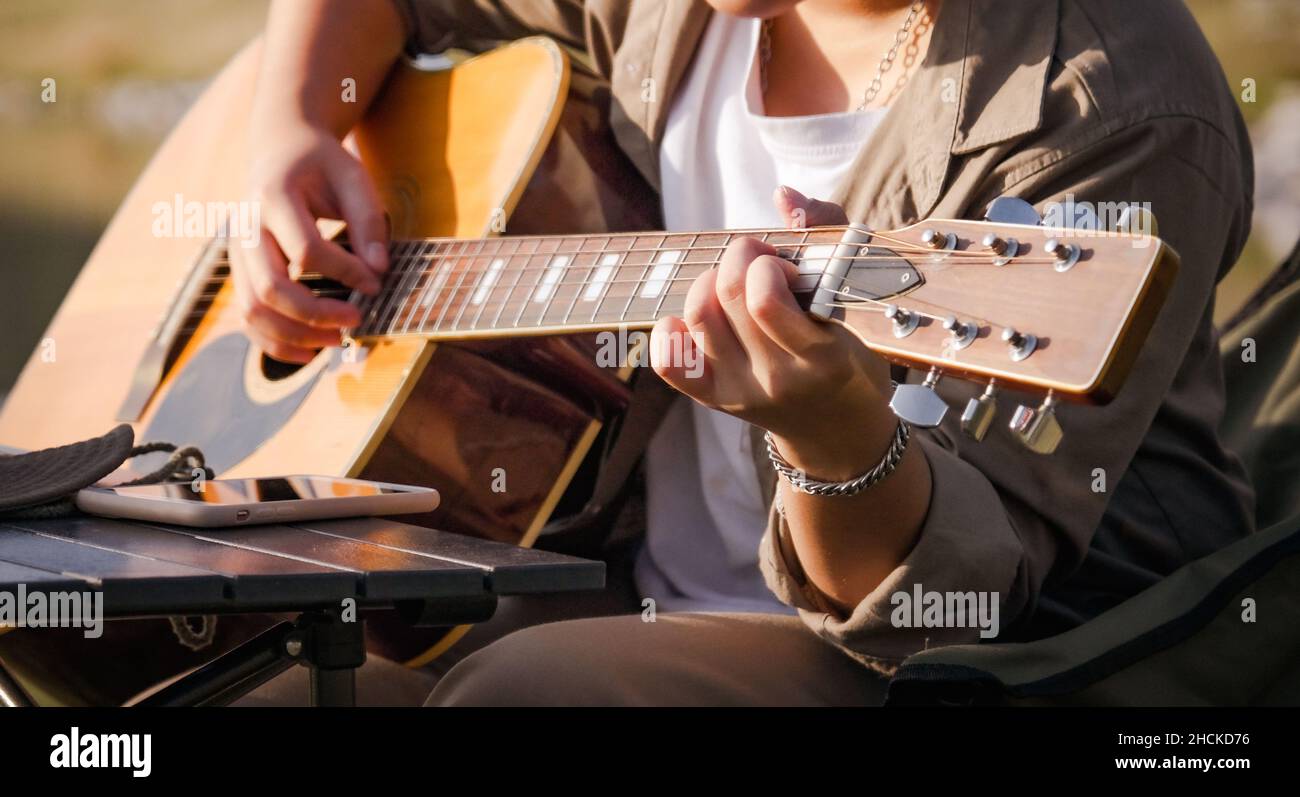 Homme jouant de la guitare à Sunset Lake, gros plan homme jouant de la main sur la guitare acoustique à l'extérieur avec la lumière du soleil réfléchie sur la surface de l'eau. Banque D'Images