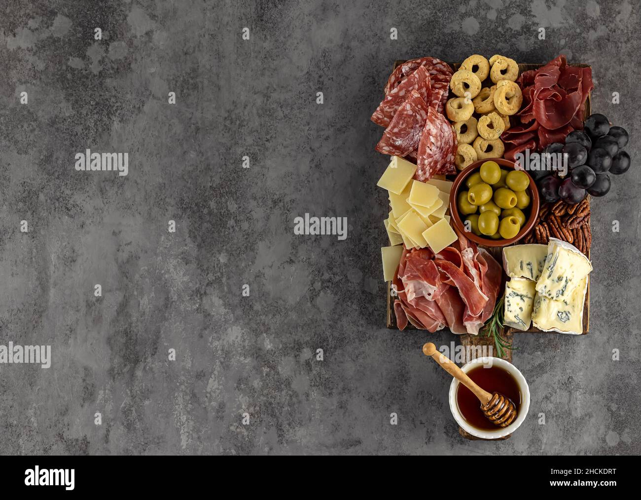 Vue de dessus d'un savoureux plateau de charcuterie avec fromage, raisin, noix, olives et jambon sur une plaque de cuisine circulaire Banque D'Images