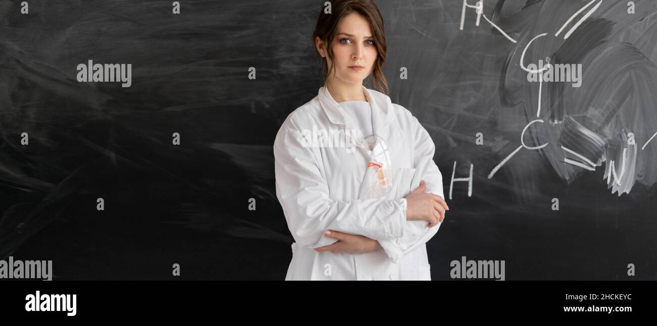 Professeur de chimie ou fille étudiante se tient contre le fond du tableau noir avec une formule chimique. Concept de retour à l'école. Banque D'Images