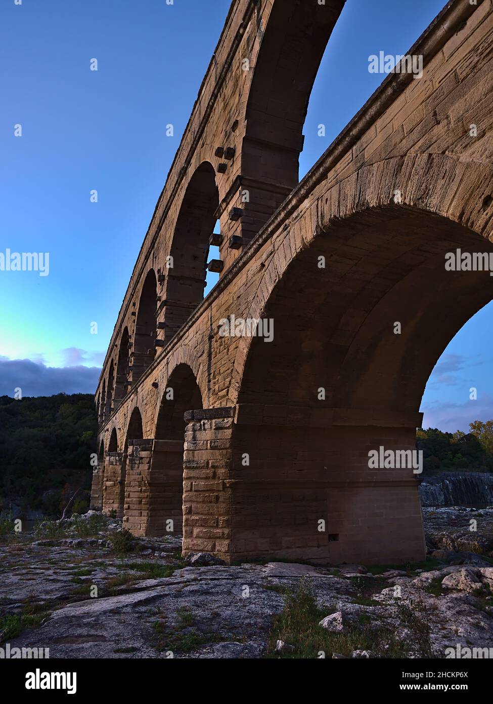 Vue latérale à angle bas de l'ancien aqueduc romain Pont du Gard avec des arches en pierre majestueuses au-dessus de la rivière Gardon après le coucher du soleil près de vers-Pont-du-Gard, France. Banque D'Images