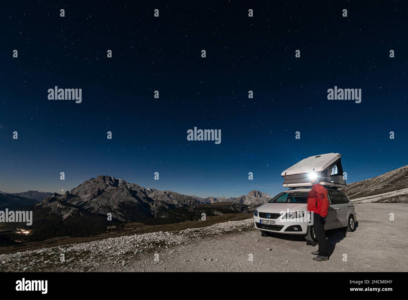Homme avec phare devant la voiture avec tente de toit sous les trois sommets avec vue sur les chaînes de montagnes et les sommets des Dolomites en clair de lune Banque D'Images