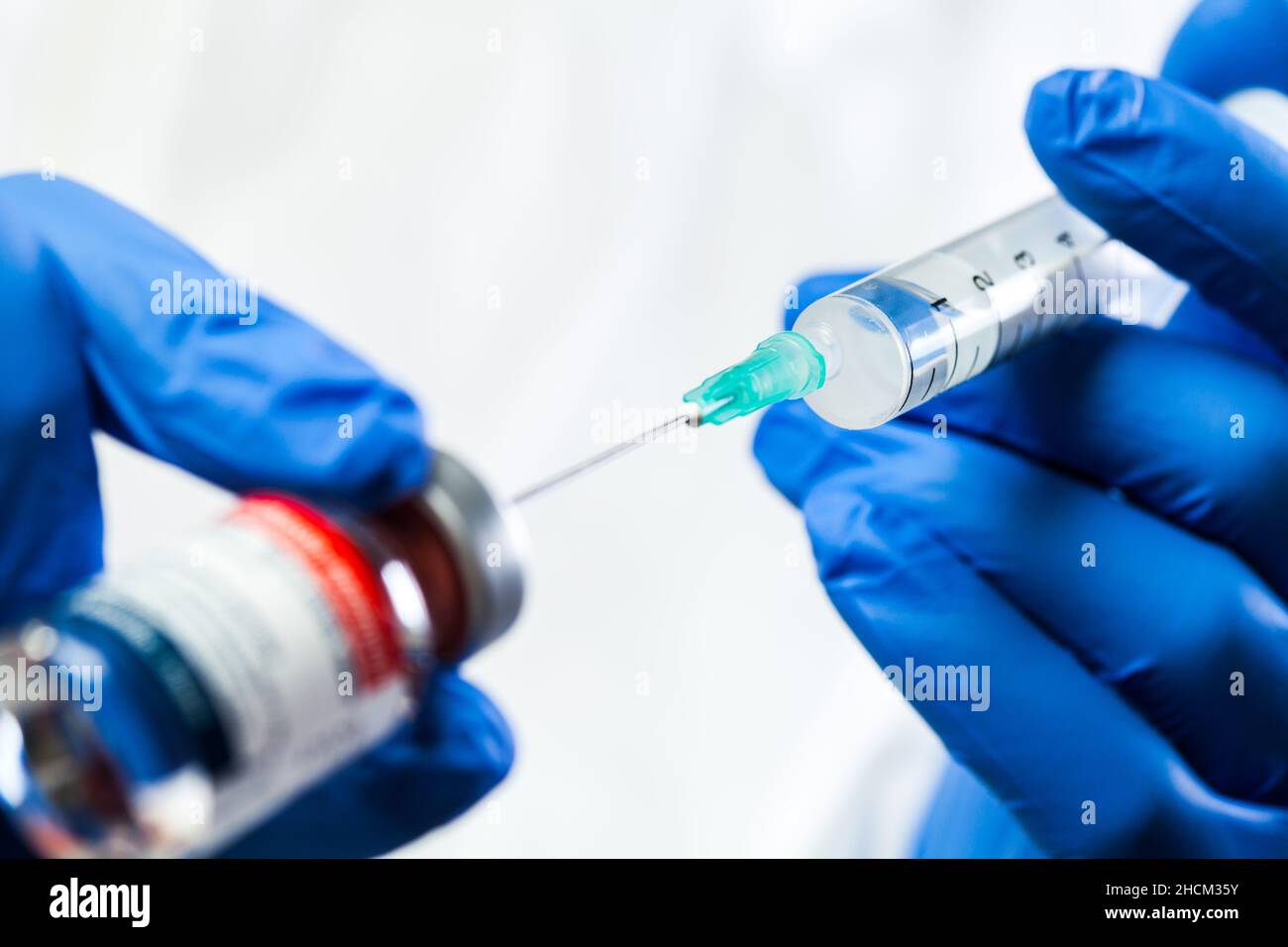 Gros plan d'un technicien médical portant des gants de protection bleus en  latex, tenant la seringue avec aiguille verte collée dans le flacon en  ampoule de verre du vaccin COVID-19 Photo Stock -