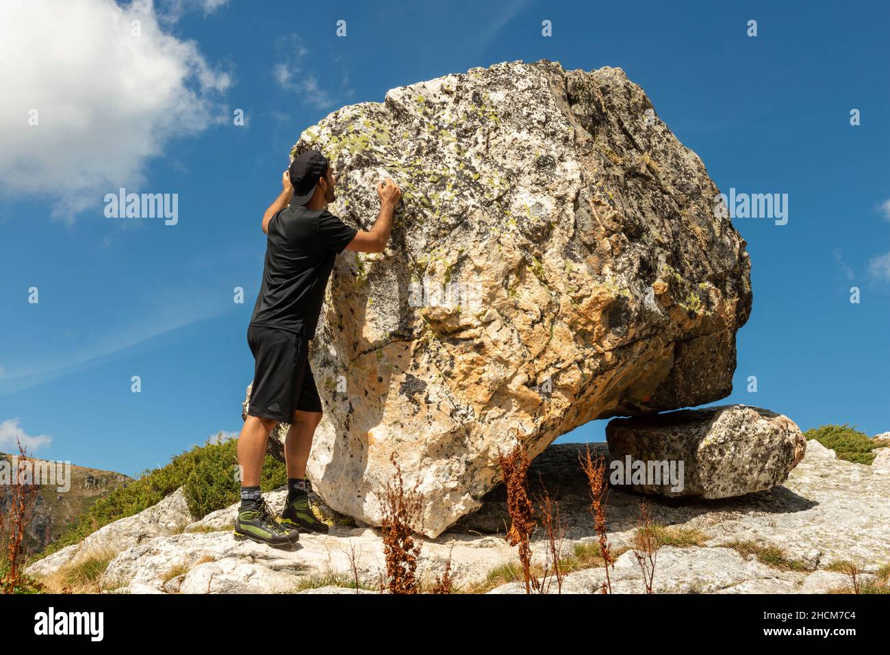 Randonneur mâle à un rocher erratique glaciaire qui équilibre sur la formation de roches de Sheepback au cirque glaciaire des sept lacs Rila, Bulgarie, Balkans Banque D'Images