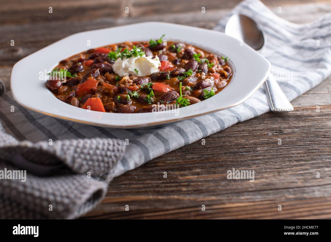 Assiette avec Chili frais cuit con carne isolée sur fond de table en bois. Surmontée de crème aigre Banque D'Images