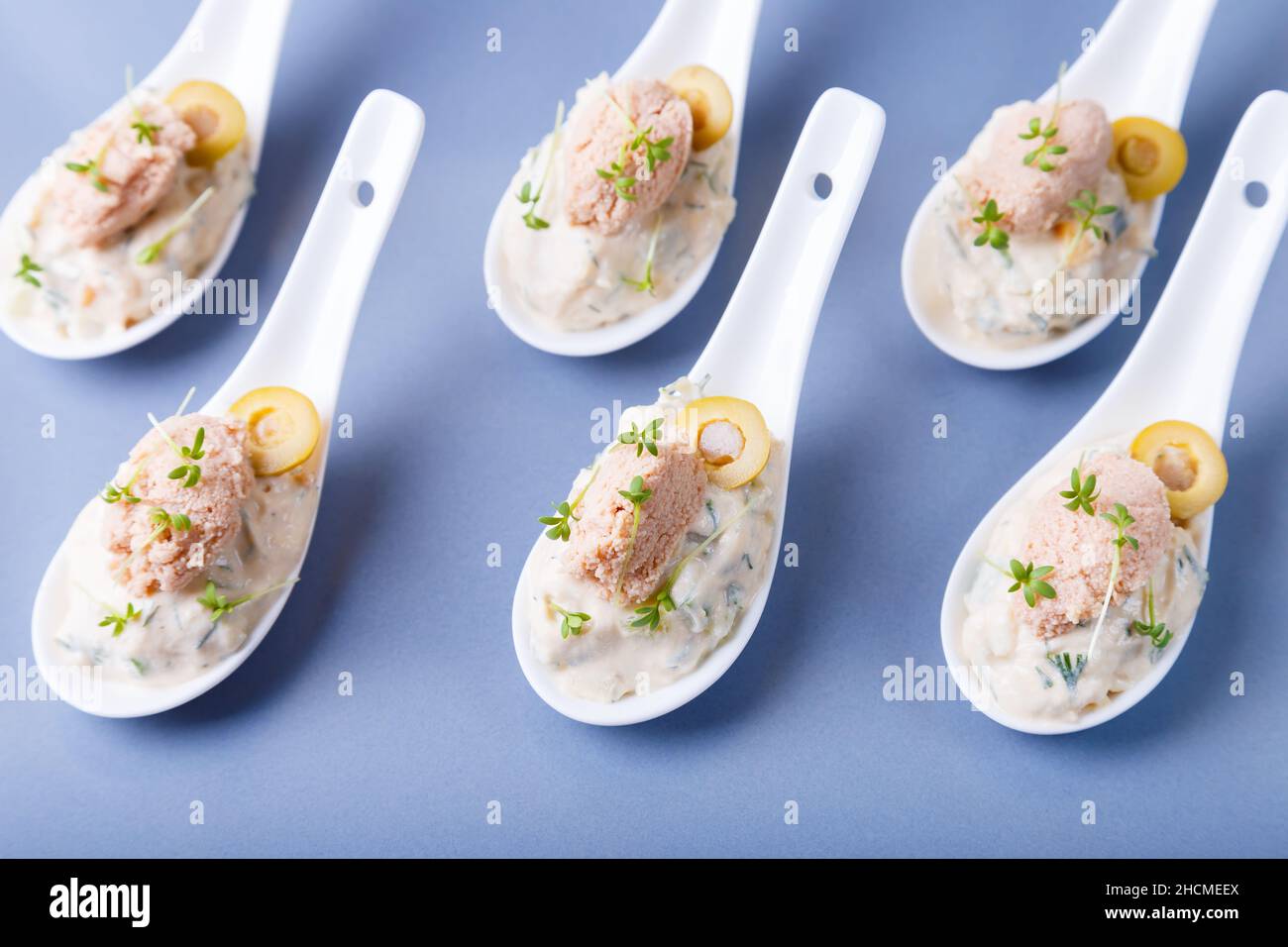 Apéritif froid à base de foie de morue, caviar de morue, olives, concombre et microverts sur les cuillères de service. Plat froid traditionnel. Gros plan, plaque bleue, noir Banque D'Images