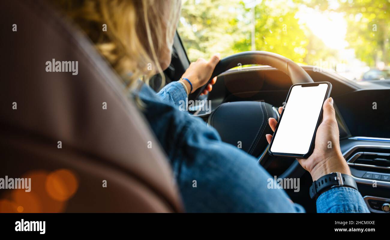 Femme tenant un téléphone portable noir dans les mains avec un écran de bureau vide pendant la conduite de voiture en été dans la ville, image de maquette Banque D'Images