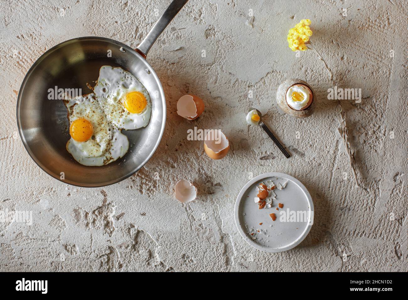 Faites frire deux œufs dans une poêle en cuivre et un œuf dur dans une tasse en grès sur fond d'argile rugueux et texturée.Concept de petit déjeuner sain. Banque D'Images