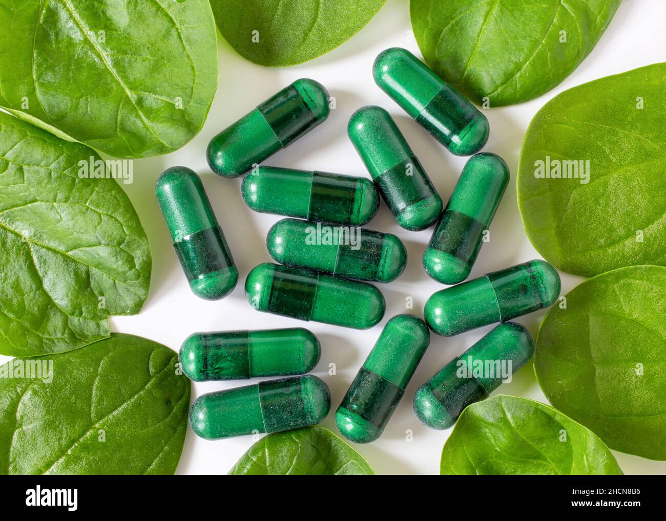 Capsules de supplément vert avec feuilles d'épinards sur blanc. Banque D'Images