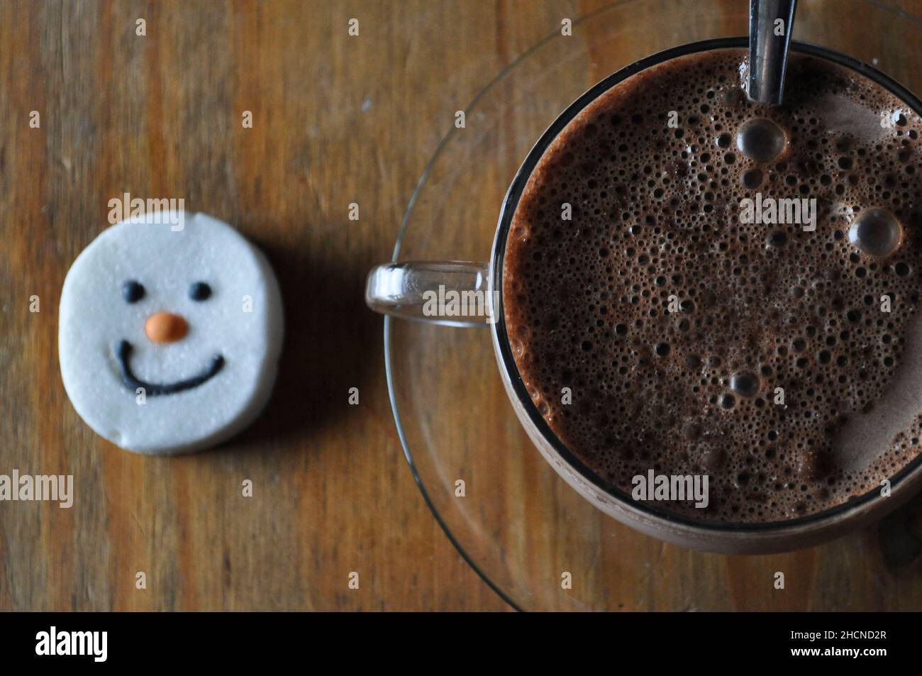 Un chocolat chaud dans une tasse en verre avec soucoupe et un guimauve à visage bonhomme de neige Banque D'Images