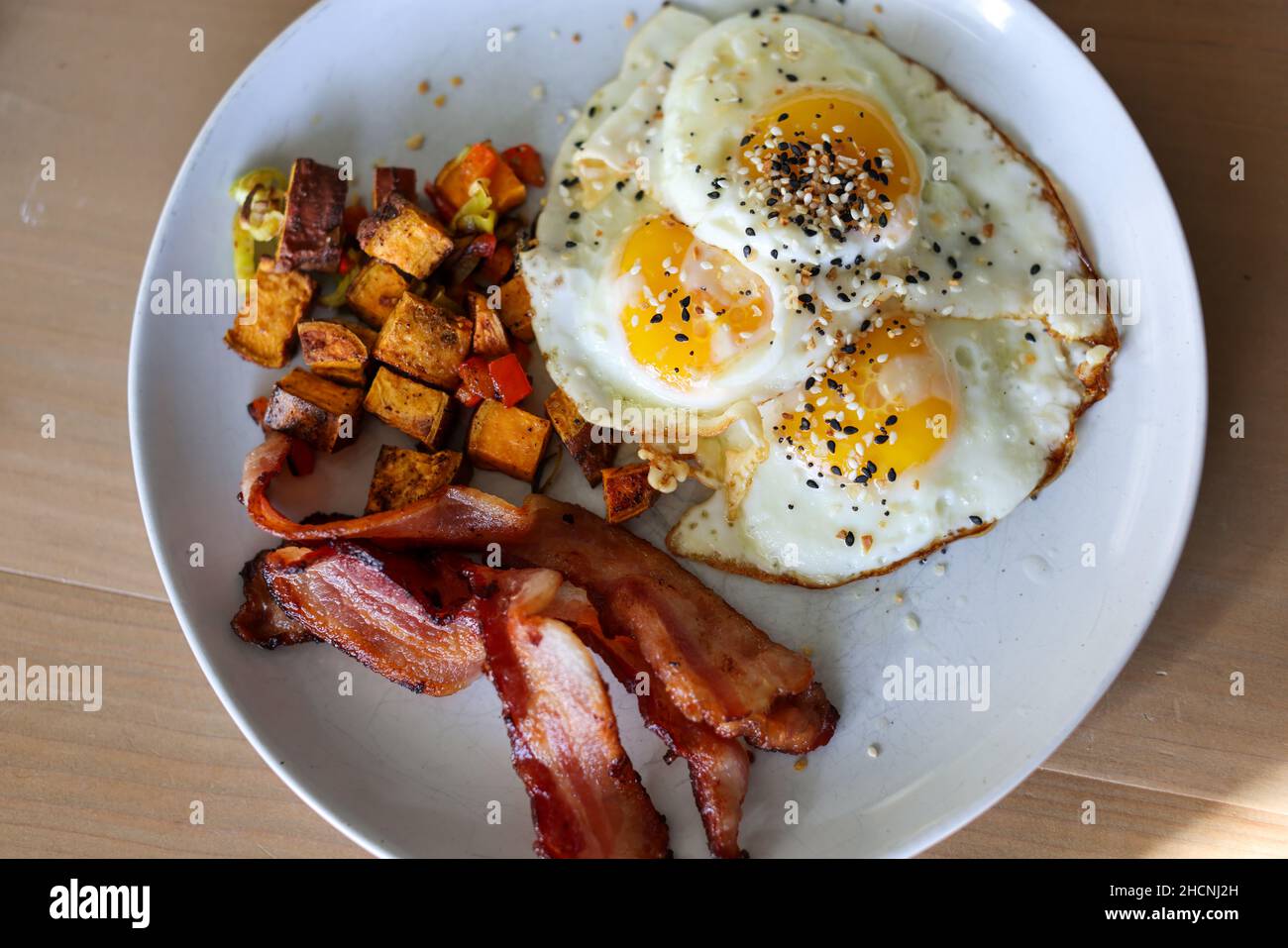 Vue de dessus des cubes de patate douce rôtis avec du bacon et des graines de sésame couvertes d'omelettes Banque D'Images