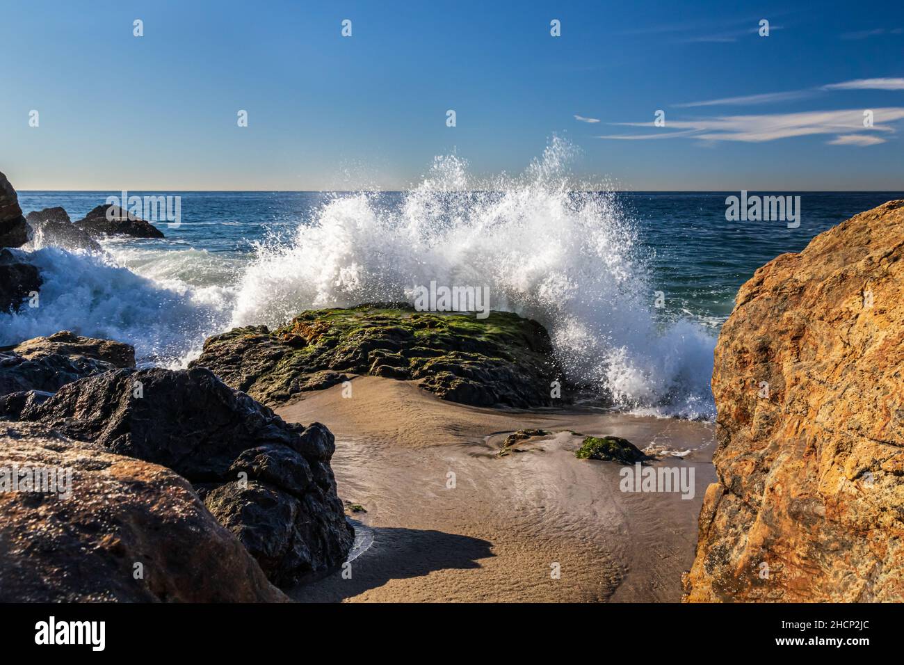 Vague de brisant la roche à Malibu, en Californie. Plage et rochers en premier plan; ciel bleu, océan Pacifique au loin. Banque D'Images