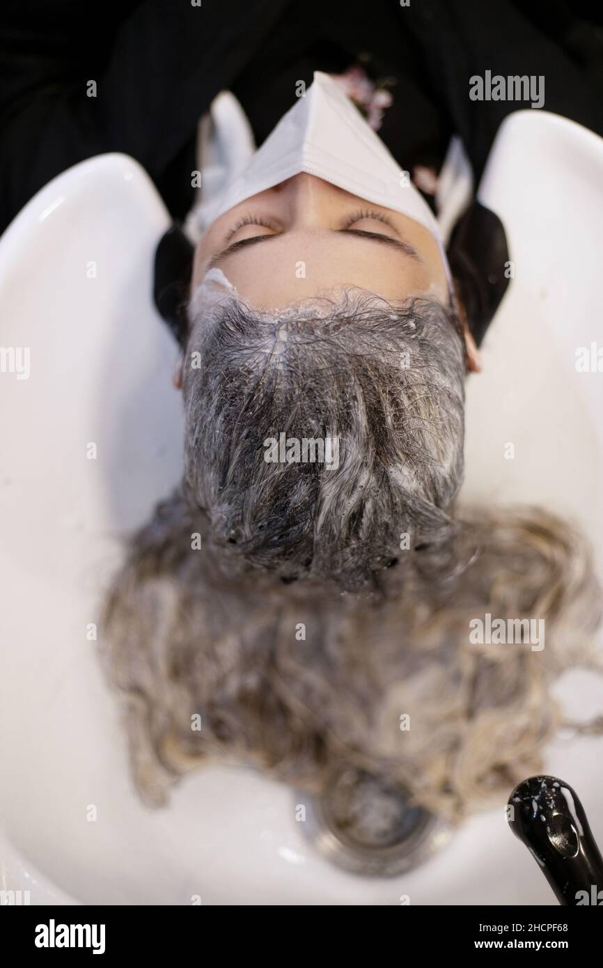 vue de dessus d'une femme avec de longs cheveux dans un lavabo de salon de coiffure et shampooing, avec masque de prévention Banque D'Images