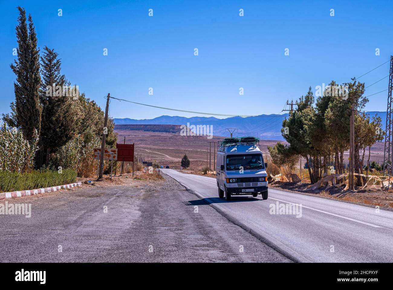 Minibus voyageant sur la route rurale par terre déserte contre le ciel bleu Banque D'Images