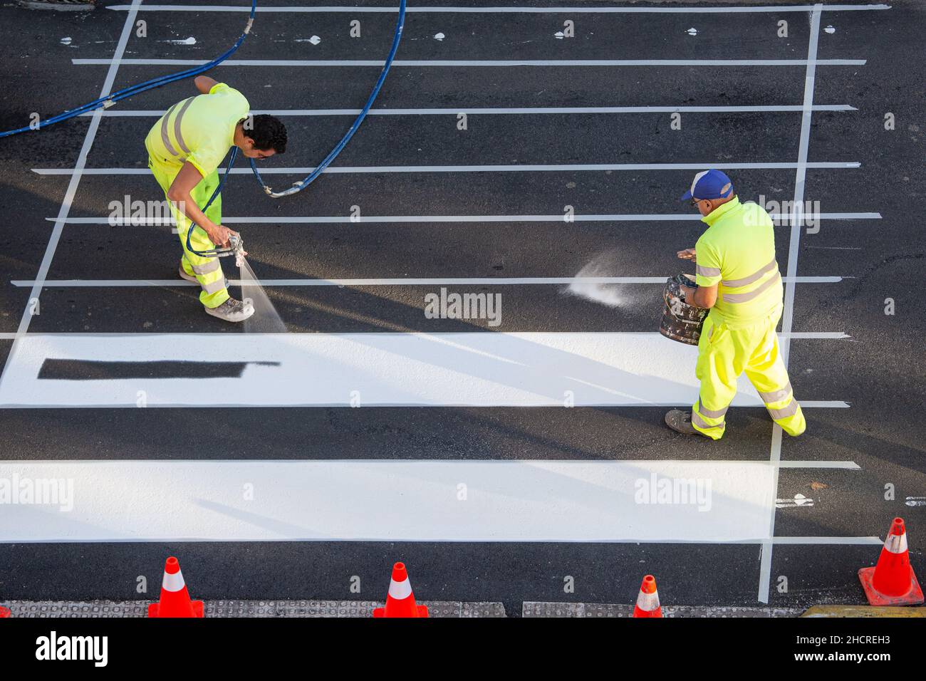 Galice, Espagne; 16 décembre 2021: Ouvriers de peinture de routes peignant des lignes d'un passage de zébré à l'aide d'un pistolet pulvérisateur de peinture Banque D'Images