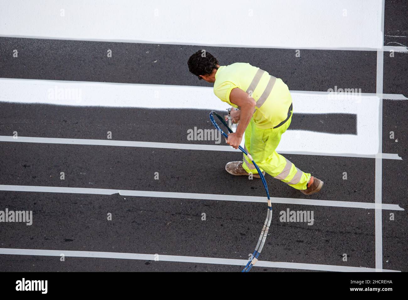 Galice, Espagne; 16 décembre 2021: Peintre de la route peinture des lignes d'un passage de zèbre à l'aide d'un pistolet pulvérisateur de peinture Banque D'Images