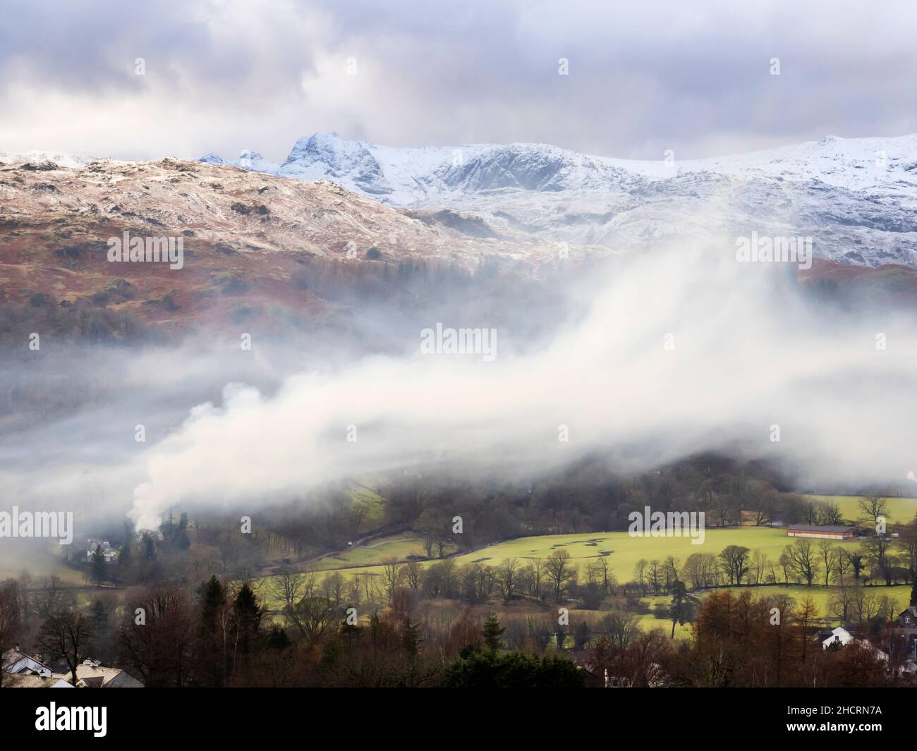 De la fumée provenant du bois vert brûlant et humide surplombe Ambleside dans le Lake District UK, tandis que les forestiers s'effacent après que Storm Arwen a explosé sur des milliers d'arbres. Banque D'Images