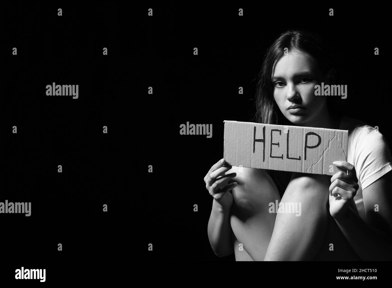 Femme effrayée tenant le papier avec l'AIDE de mot sur fond sombre.Concept de violence Banque D'Images