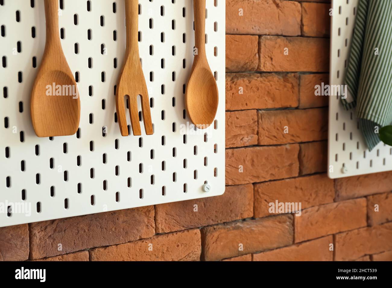 Panneau perforé avec spatules en bois accrochées sur un mur en brique Banque D'Images
