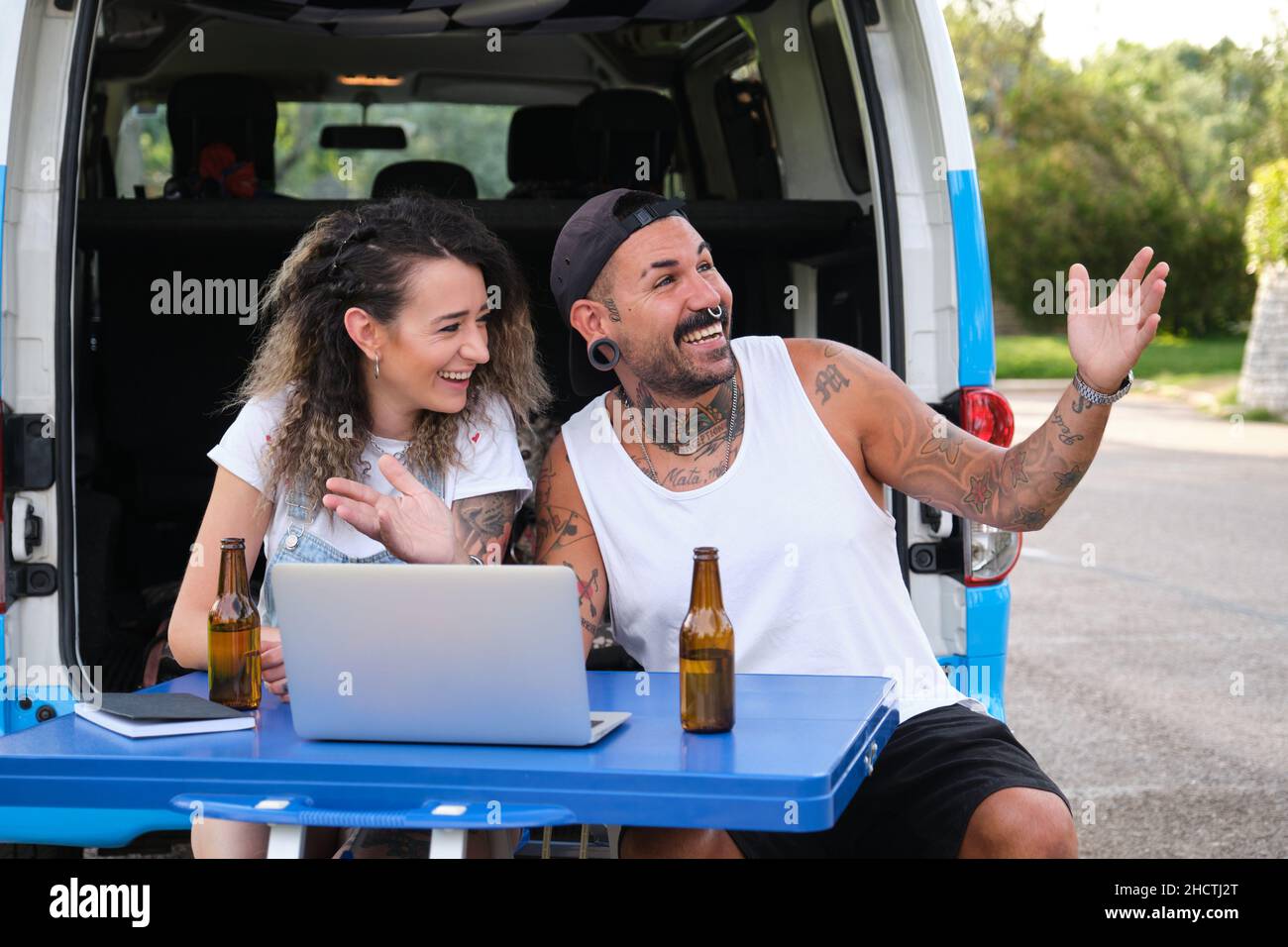 Un jeune couple tatoué sourit et parle lors d'un appel vidéo sur ordinateur portable pendant un voyage en minibus. Banque D'Images