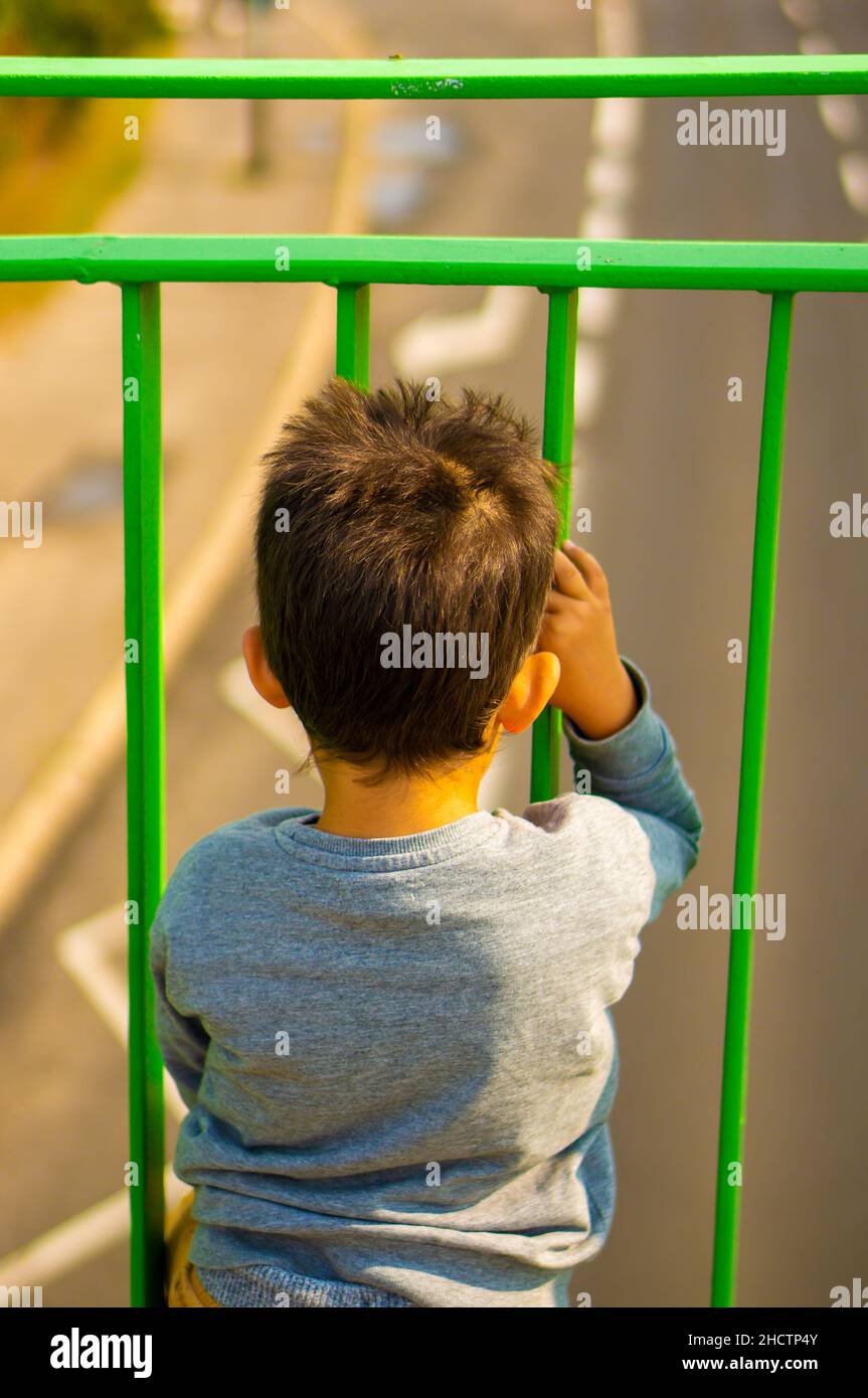 Photo verticale d'un jeune garçon caucasien regardant des voitures sur une route depuis l'arrière d'une barrière Banque D'Images