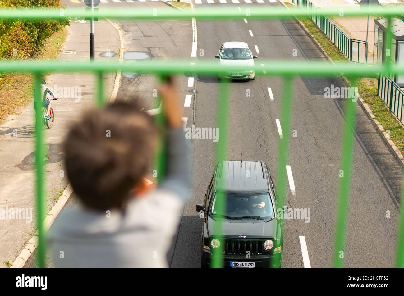 Un jeune garçon regarde les voitures sur une route depuis l'arrière d'une barrière Banque D'Images